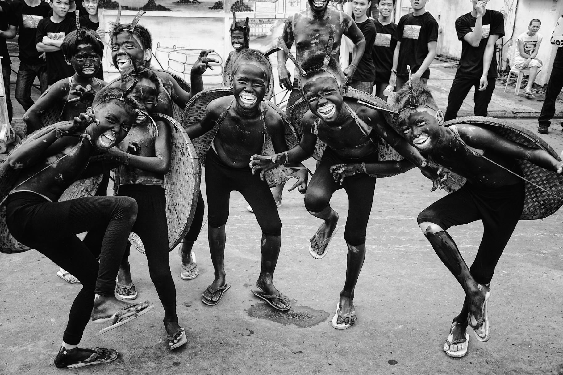 Black and white frame of laughing Ati-Atihan boys with soot-painted bodies and woven shields