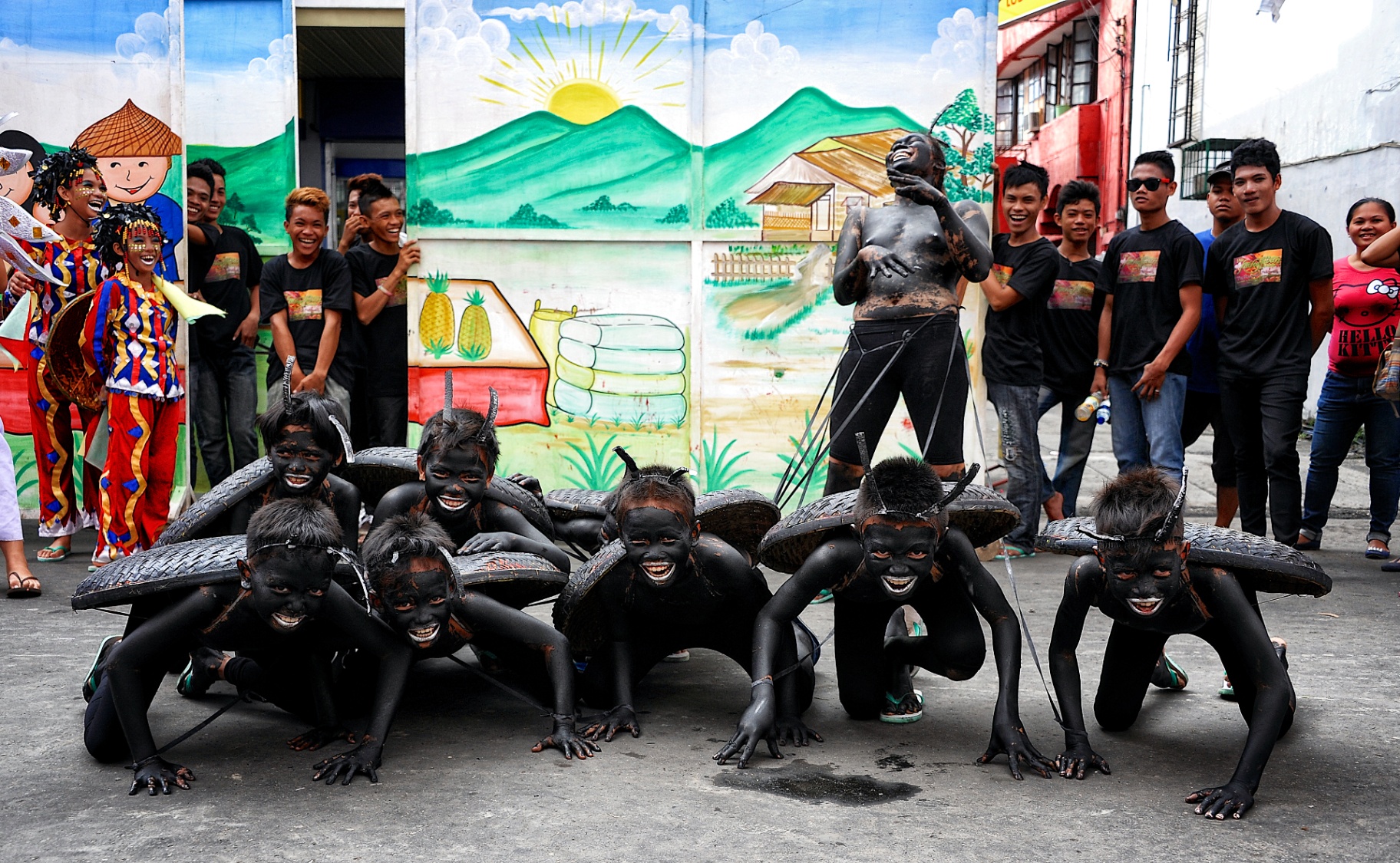 Ati-Atihan troupe of soot-painted boys posed in front of a hand-painted village mural