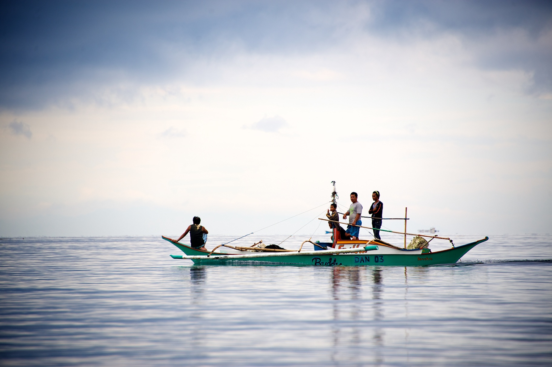 Filipino fishermen on a traditional bangka outrigger on a glassy sea