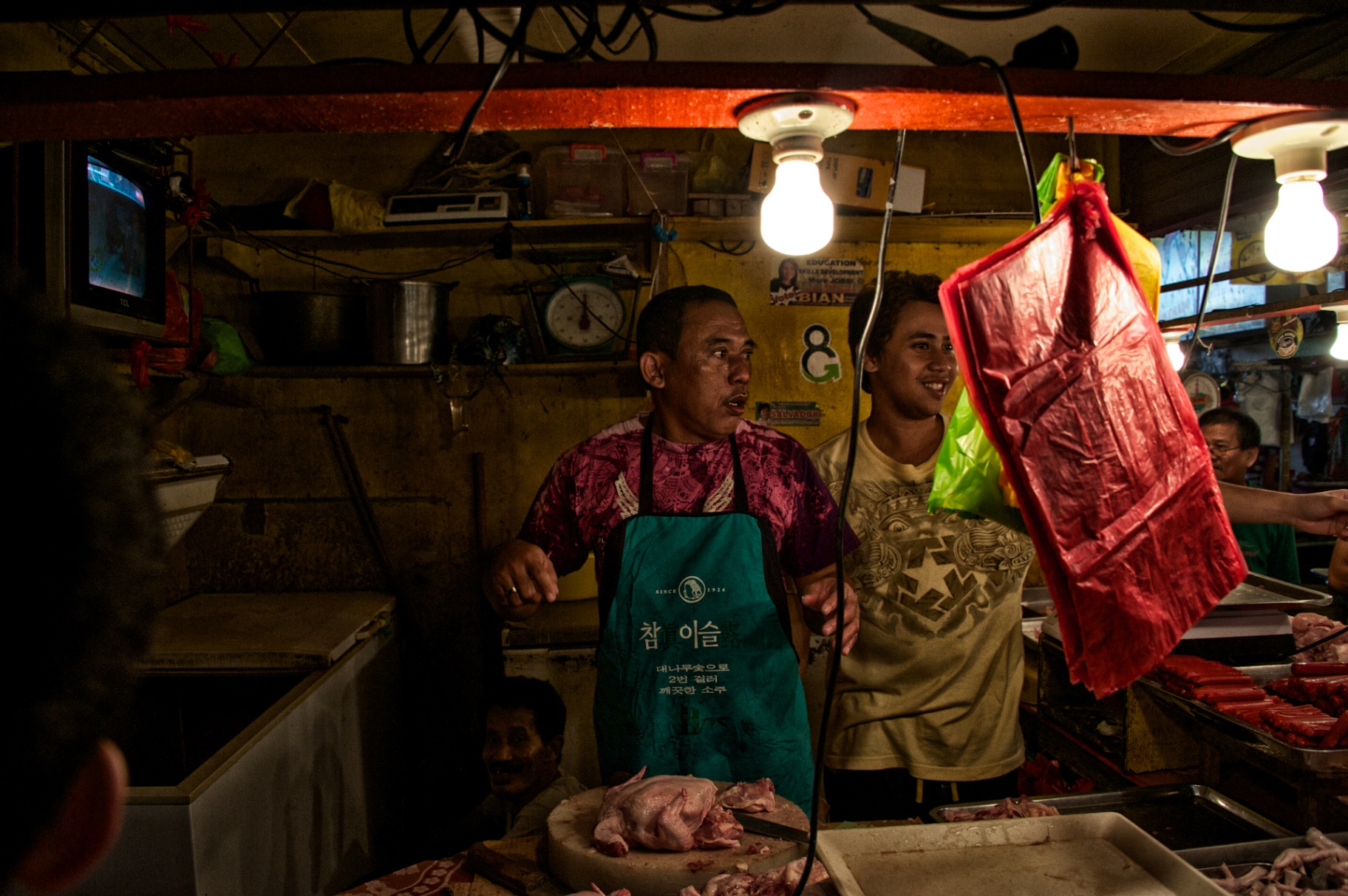Two Filipino butchers behind their counter, lit by hanging bulbs