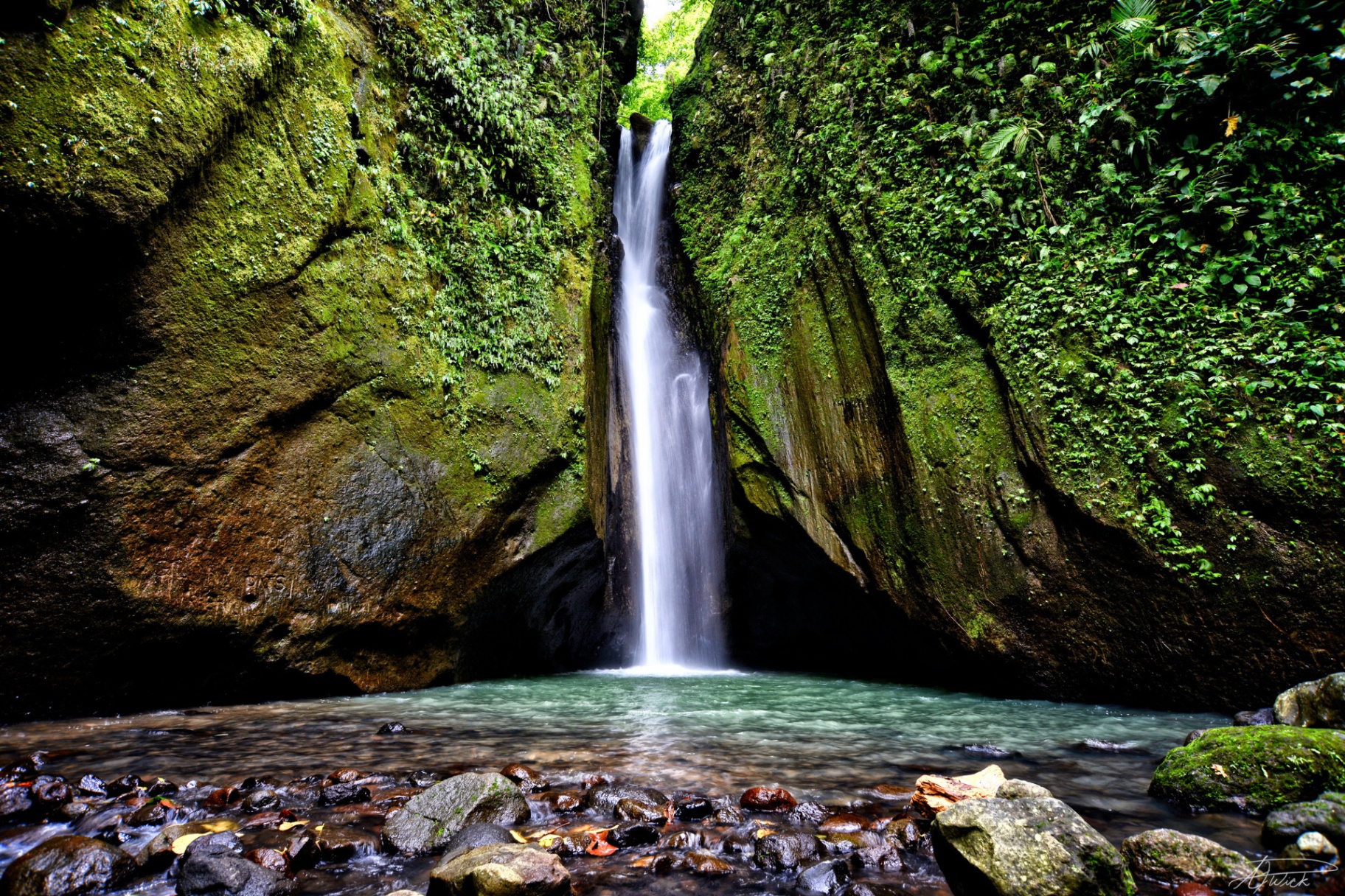 Tall waterfall pouring between mossy canyon walls into a turquoise pool, Philippines