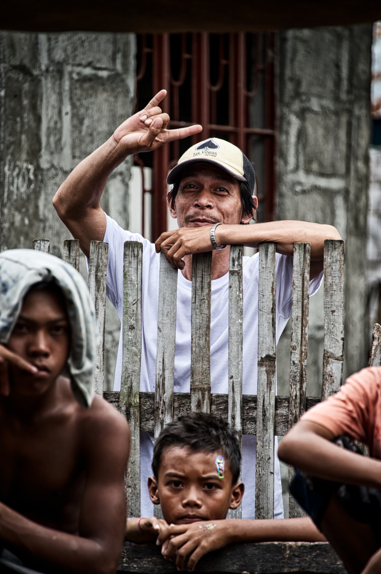 Filipino father in a white shirt and cap leaning over a bamboo fence with his two sons in the foreground