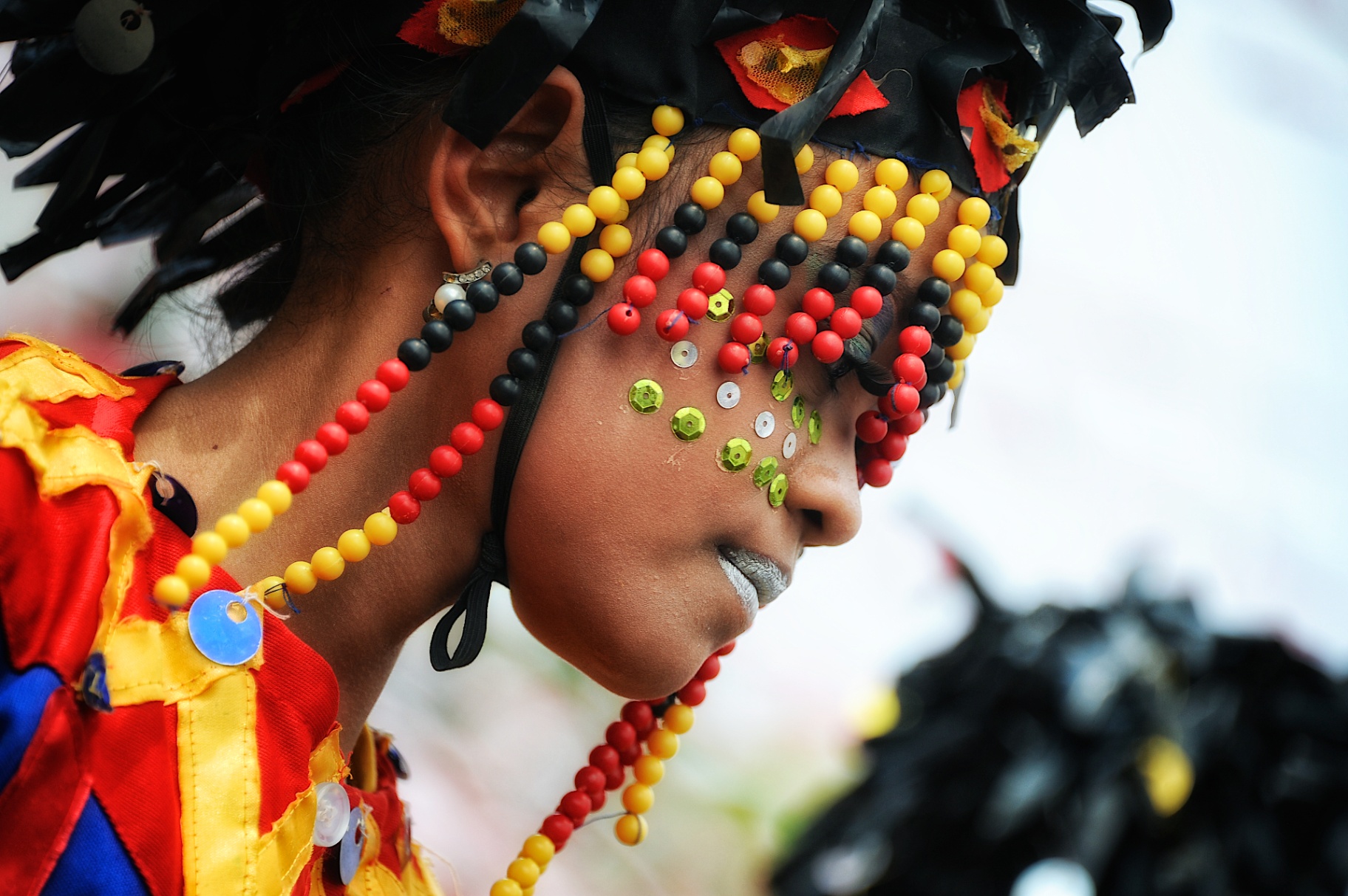 Close-up profile of a Filipina festival dancer adorned with red, yellow and black beadwork and sequins