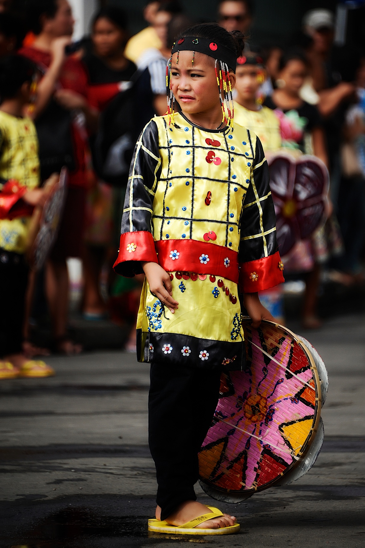 Young Filipina girl in yellow beaded festival costume holding a painted woven shield