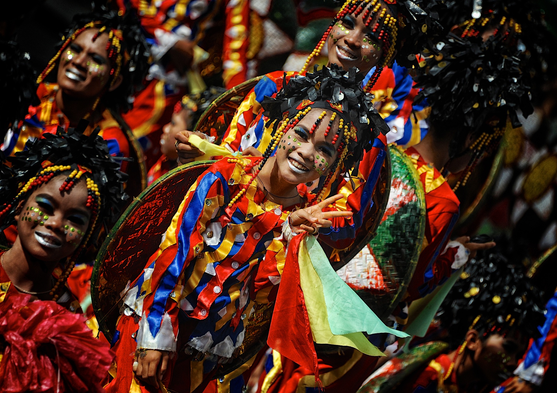 Joyful Filipina festival dancer in red, blue and yellow costume flashing a peace sign at Ati-Atihan
