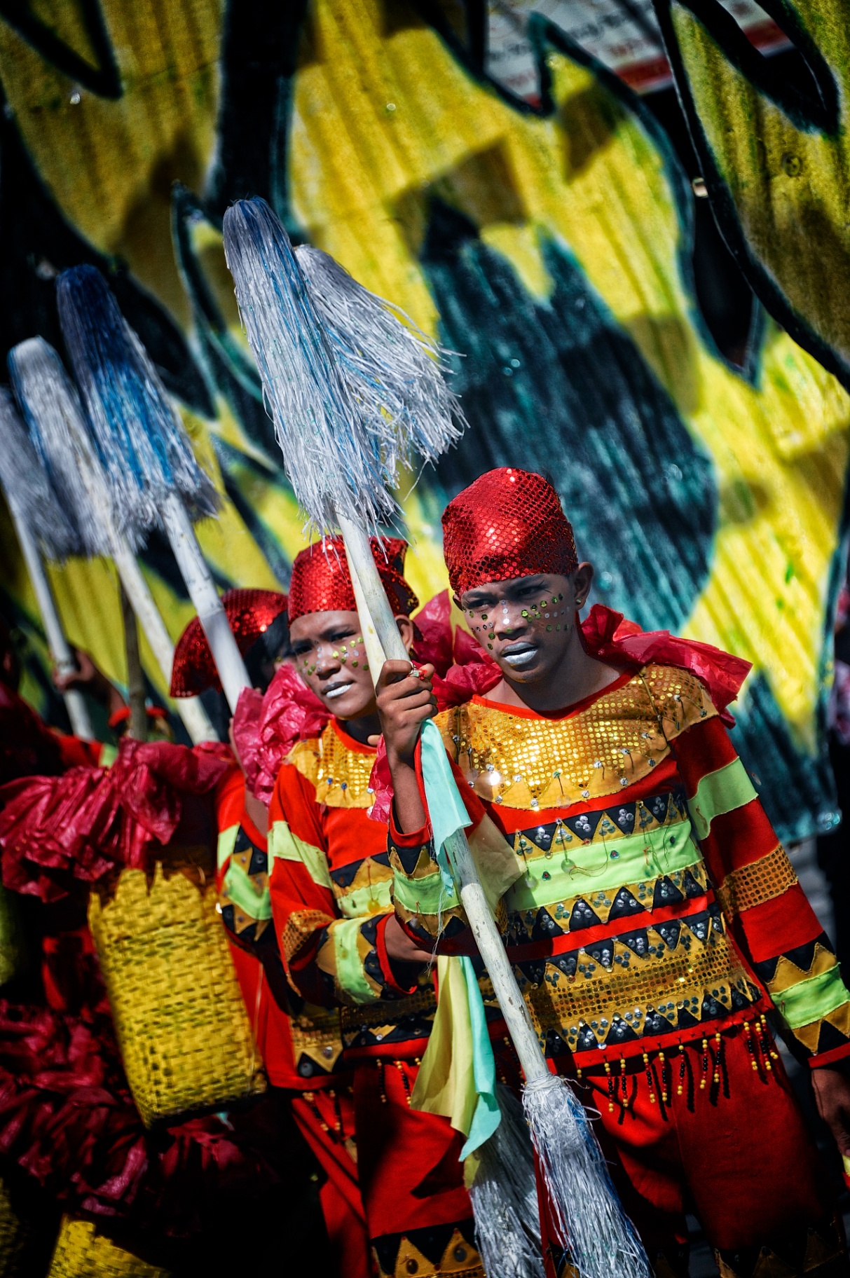 Two young Filipino festival dancers in red sequined caps and striped costumes holding tasselled staffs