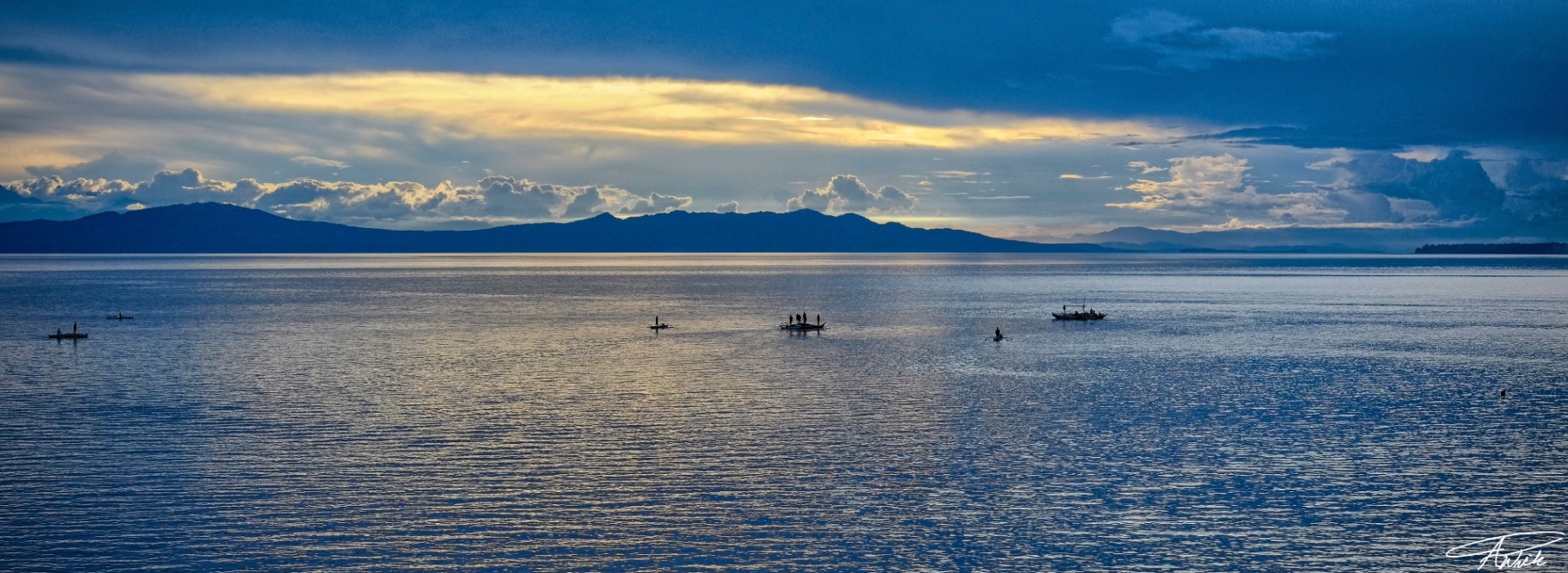 Panoramic silhouettes of Filipino fishermen on bangkas across a silver sea beneath a luminous cloudbreak