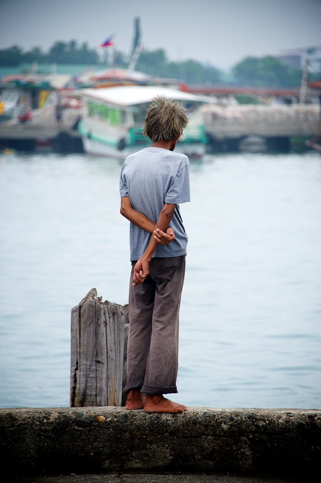 Barefoot boy with sun-bleached hair watching boats in a Philippine harbor
