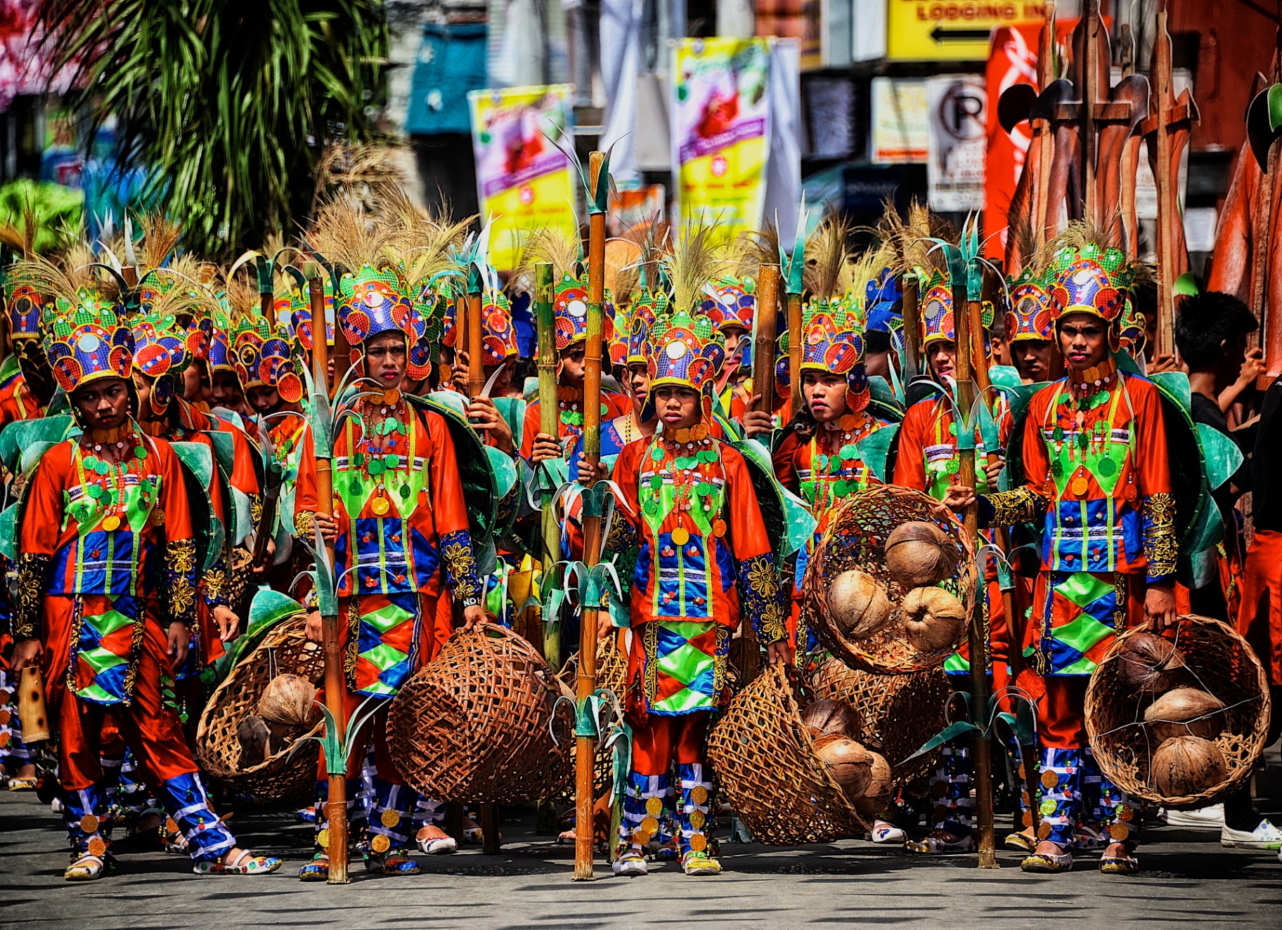 Ati-Atihan harvest troupe in orange, blue and green costumes carrying baskets of coconuts and bamboo