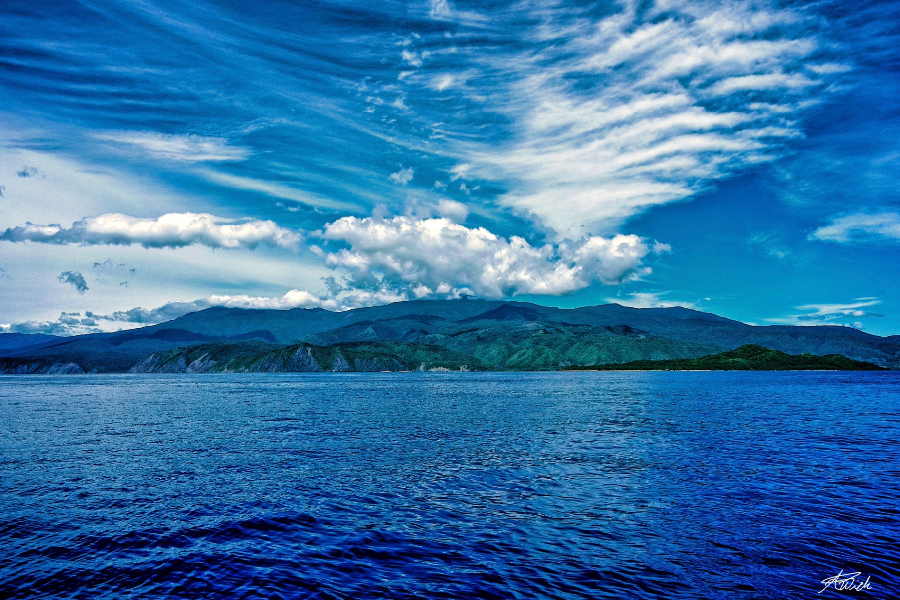 Deep blue sea stretching toward a mountain island under dramatic cloud forms