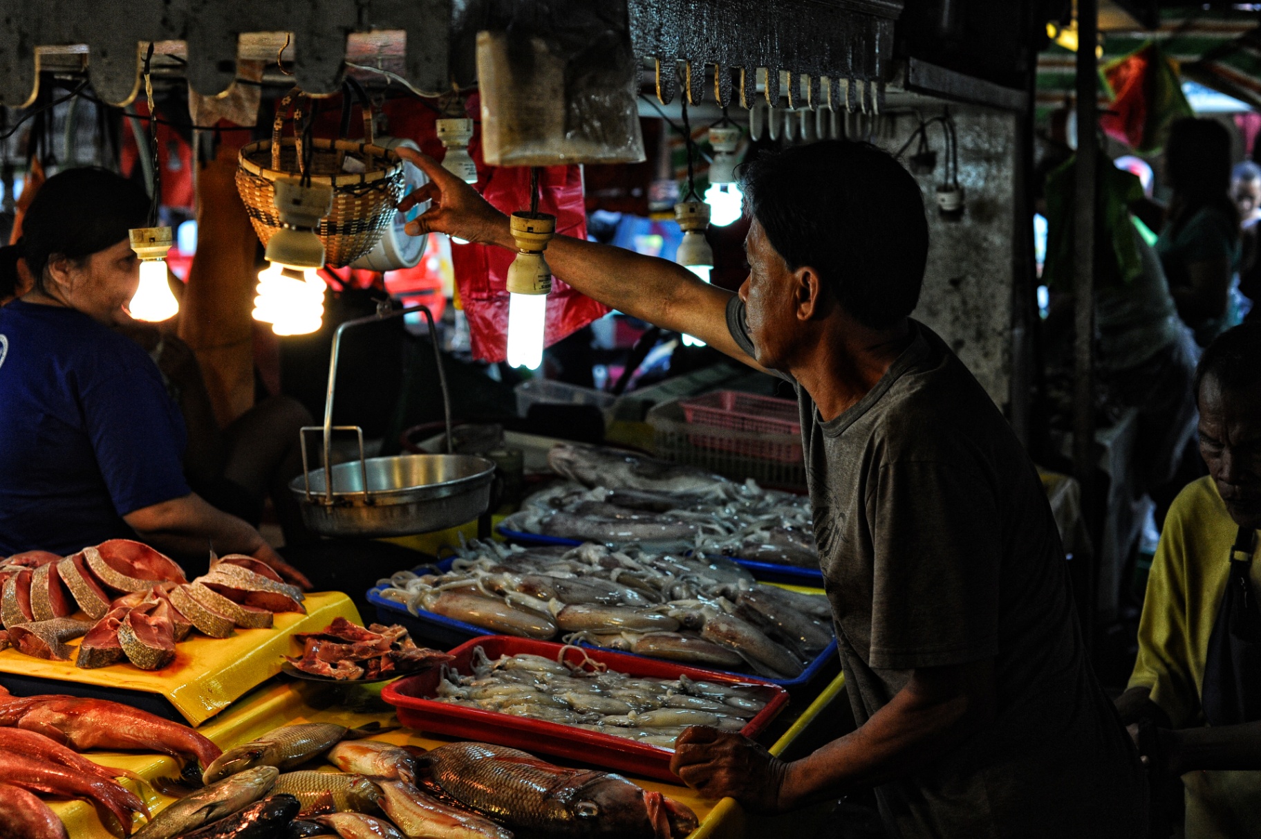 Fish vendor adjusting a hanging lamp at a Philippine market