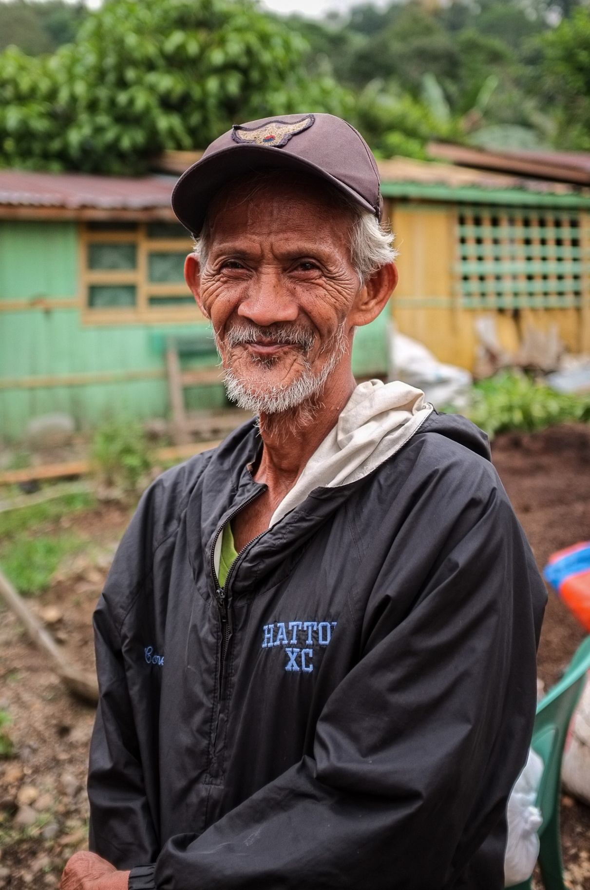 Smiling Filipino elder standing outside his village home