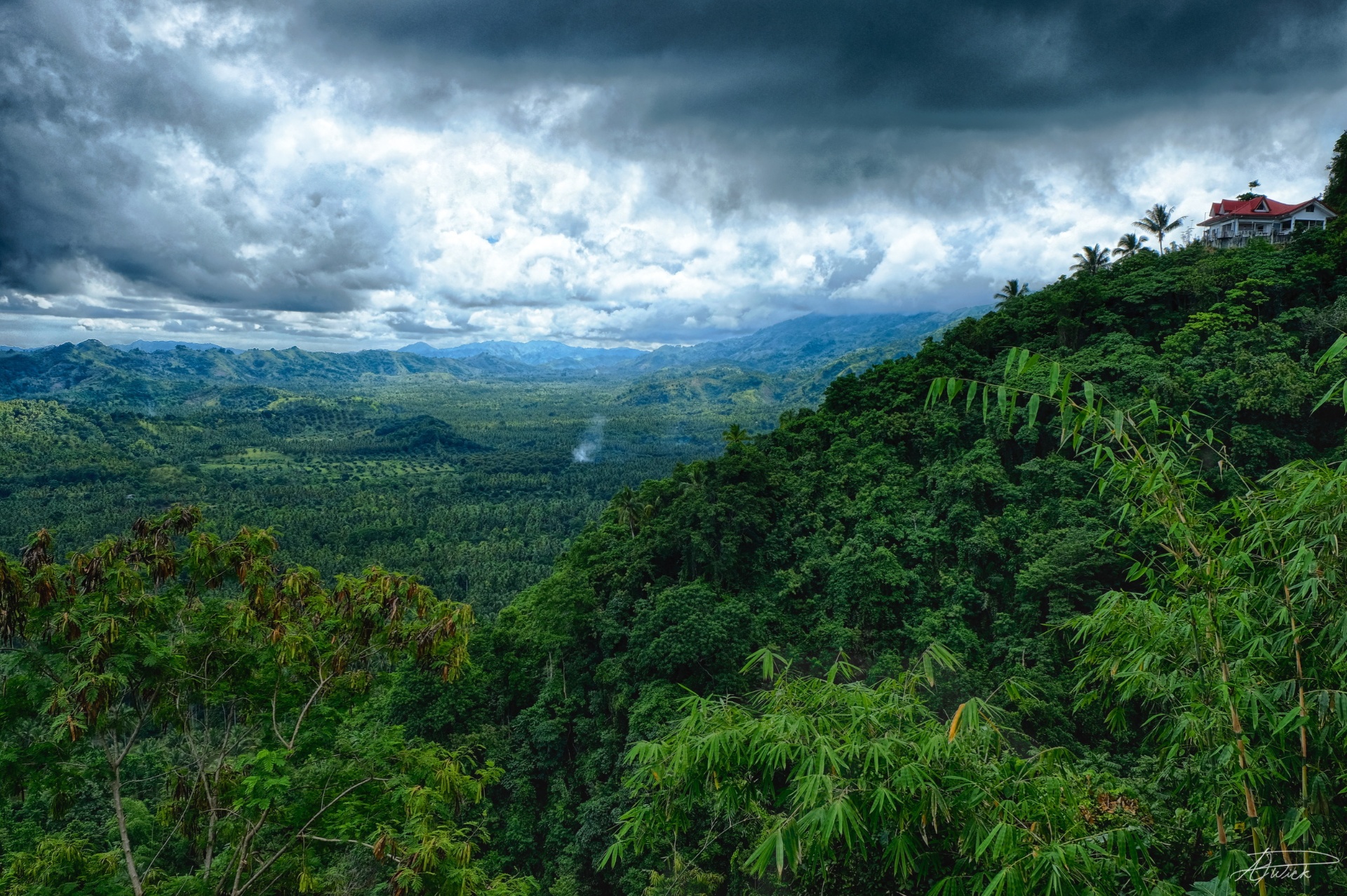 Red-roofed Filipino home perched on a jungle ridge above a vast valley beneath dramatic storm clouds