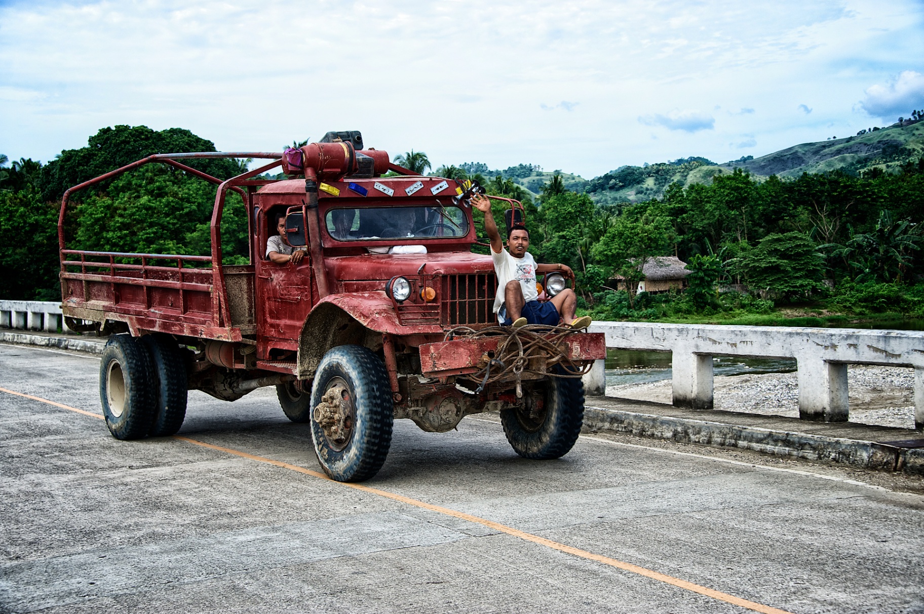 Vintage red Philippine truck crossing a concrete bridge with a young man riding the bumper