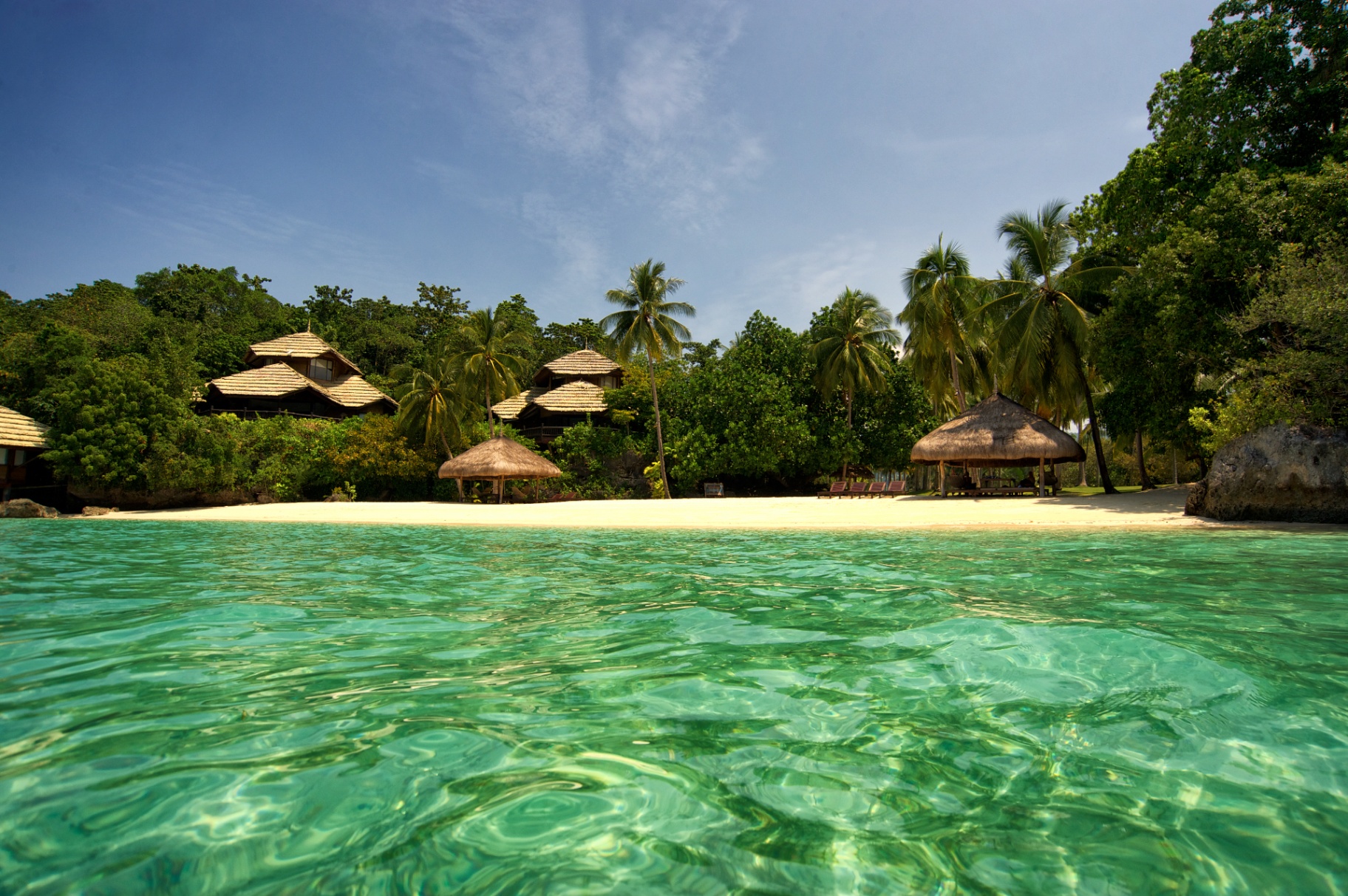 Emerald cove with thatched bungalows and palms behind a white sand beach in the Philippines