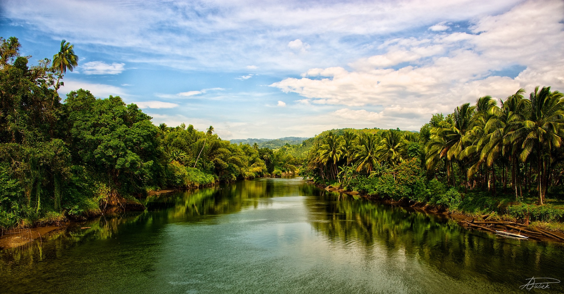 Wide river bending through palm-lined jungle under a cloud-streaked Philippine sky