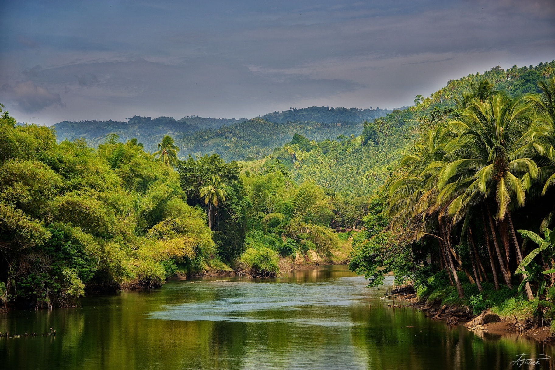Mirror-still river leading toward forested mountains in the Philippines