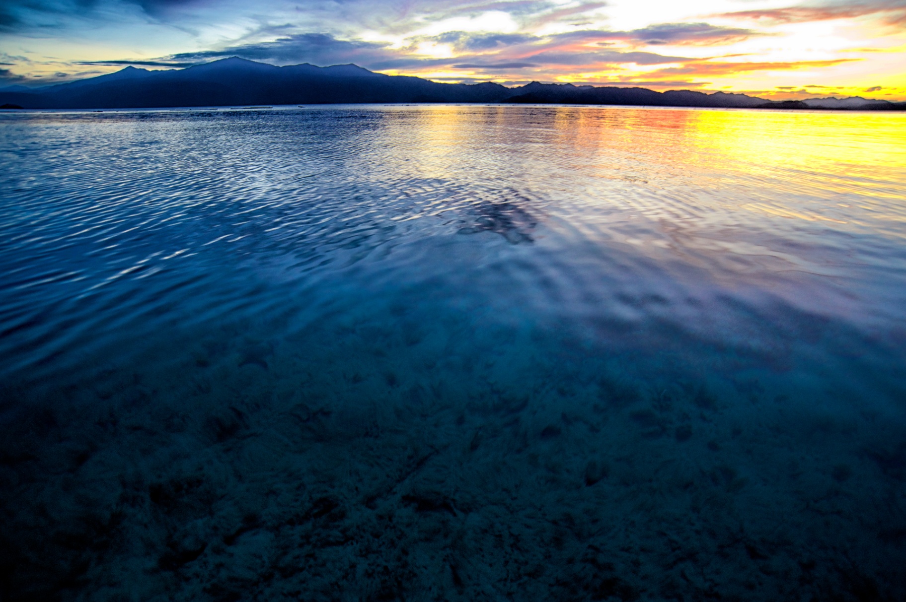 Sunset over rippled shallows with distant mountains, Philippines