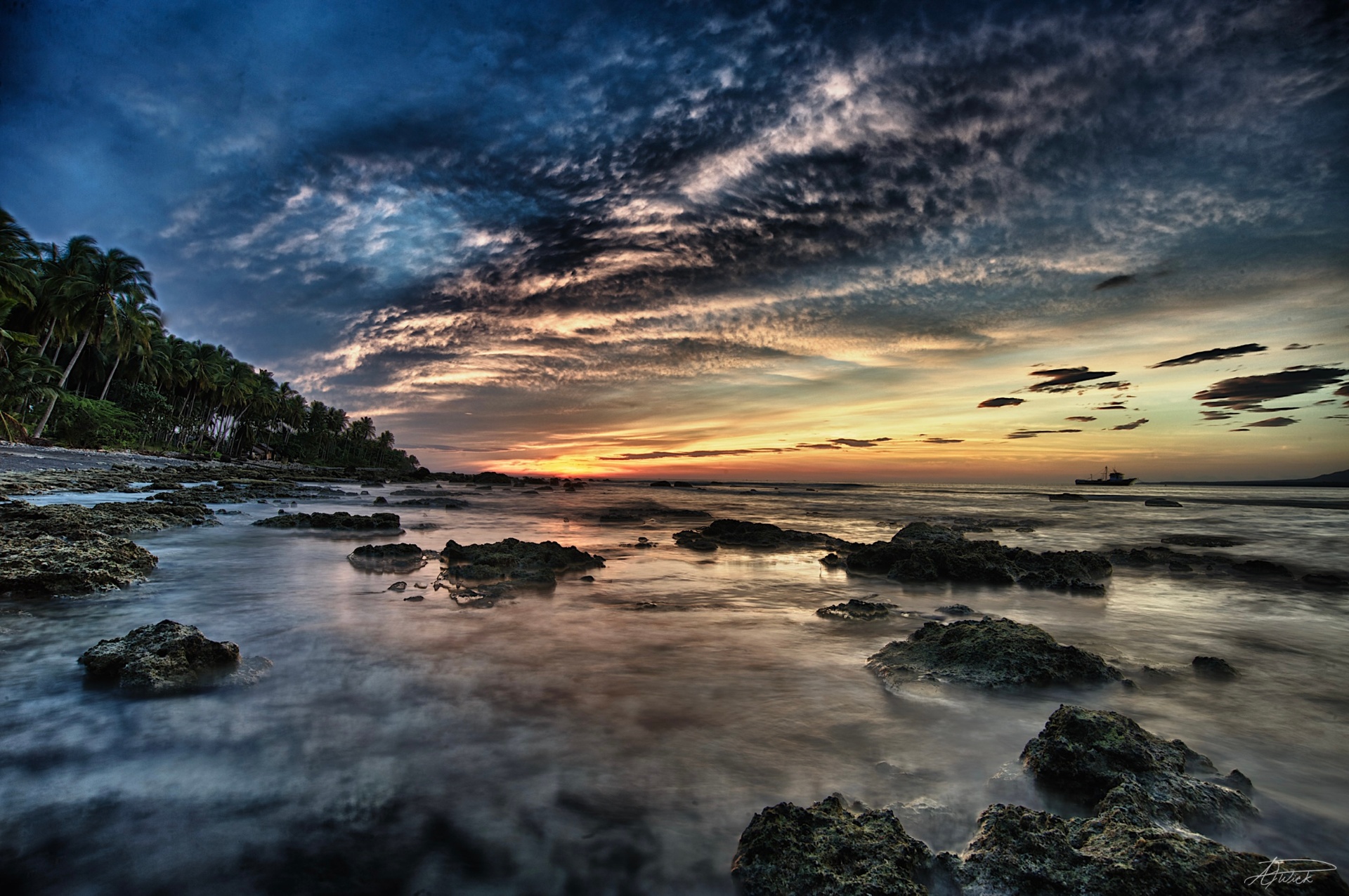 HDR sunset over a rocky tidepool shore with palms and a distant cargo ship, Philippines