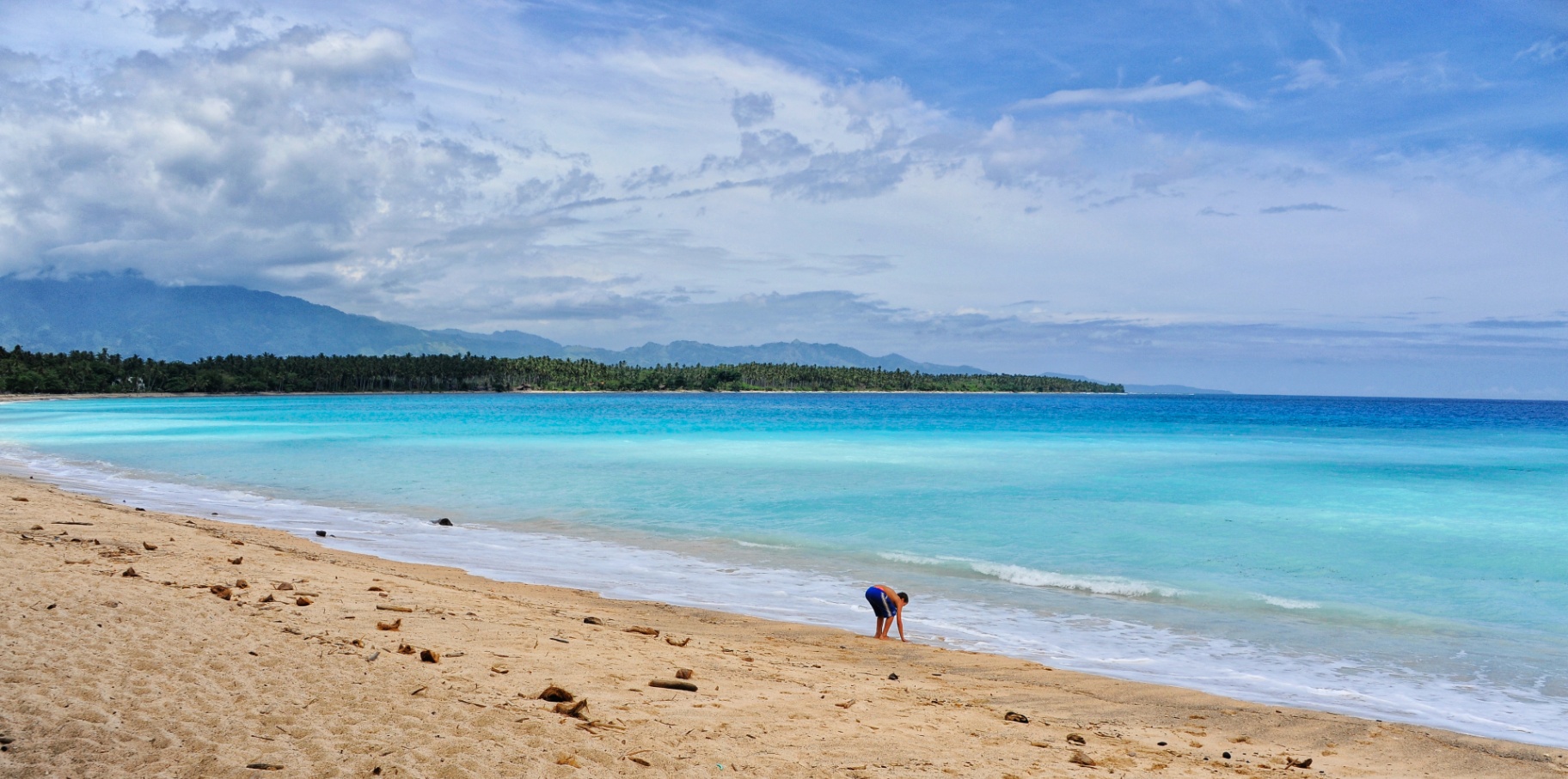 Child playing on a vast turquoise bay shoreline in the Philippines