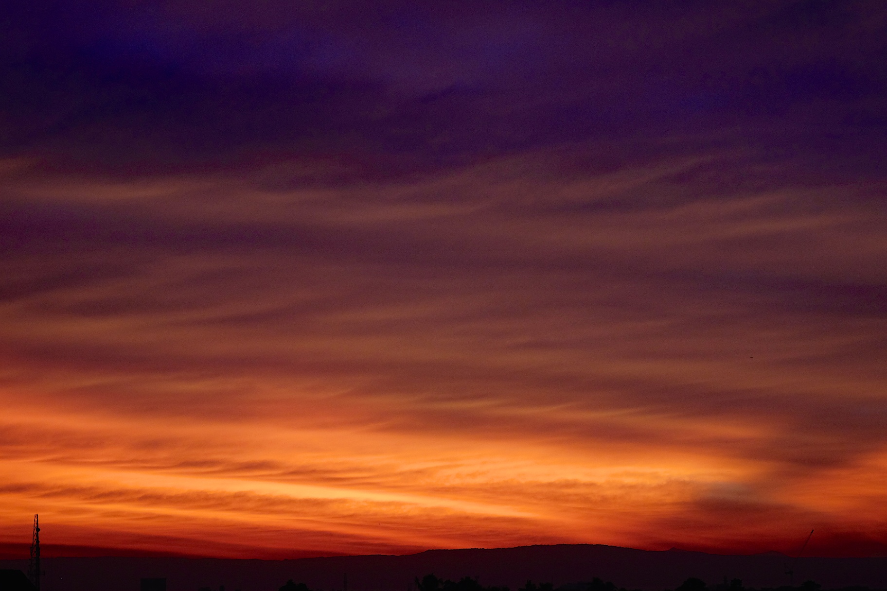 Violet and burnt orange sunset clouds layered above a dark mountain silhouette