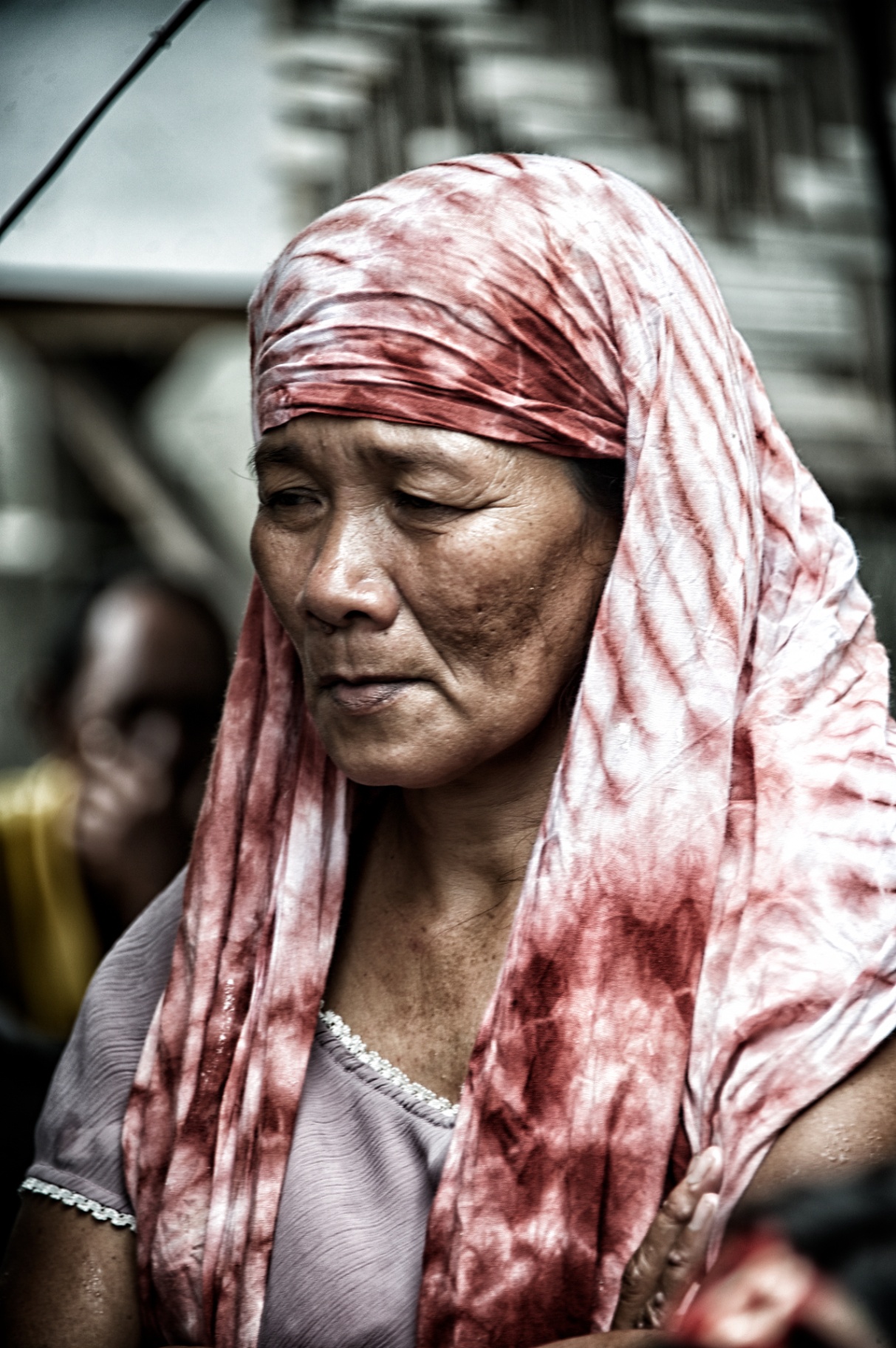 Filipina market woman wearing a crimson tie-dyed headscarf, eyes lowered in quiet thought